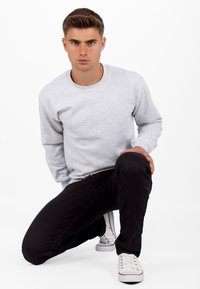 Grijze sweatshirt met ronde hals, lange mouwen en een gestructureerde stof. Gemaakt met zwarte broek en witte sneakers met rode accenten.