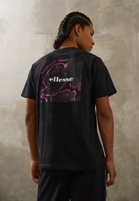 Black t-shirt featuring a stylized pink and black graphic and "ellesse" logo on the back. Short sleeves and casual fit.
