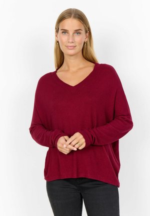Burgunderfarbener V-Ausschnitt-Pullover, lange Ärmel, weicher Stoff, lockere Passform, mit Rippbündchen, kombiniert mit dunklen Jeans. Einfaches und vielseitiges Design.