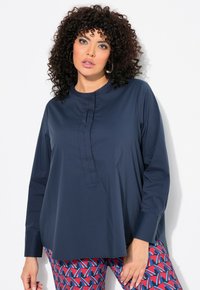 Marineblaue langärmlige Bluse mit rundem Halsausschnitt, ausgestattet mit einer vertikalen Knopfleiste mit roten Akzenten. Glatte Textur und lockerer Schnitt.