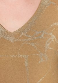 Bronzový svetr s výstřihem do V, který má texturovaný, metalicky stříbrný abstraktní vzor na hladké, přiléhavé látce. Subtilní lesk dodává hloubku.