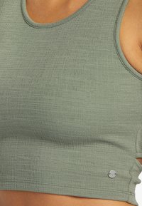 Vihreä, teksturoitu urheil bra, jossa on pyöreä pääntie. Mukana hopeinen logoyksityiskohta sivulla ja Slim-fit muotoilu.