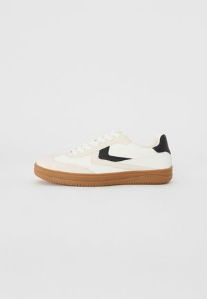 Fehér és krém színű sneakers fekete részletekkel, gumiból készült talppal, sima textúrával, lekerekített orral és egyszerű fűzős kialakítással.