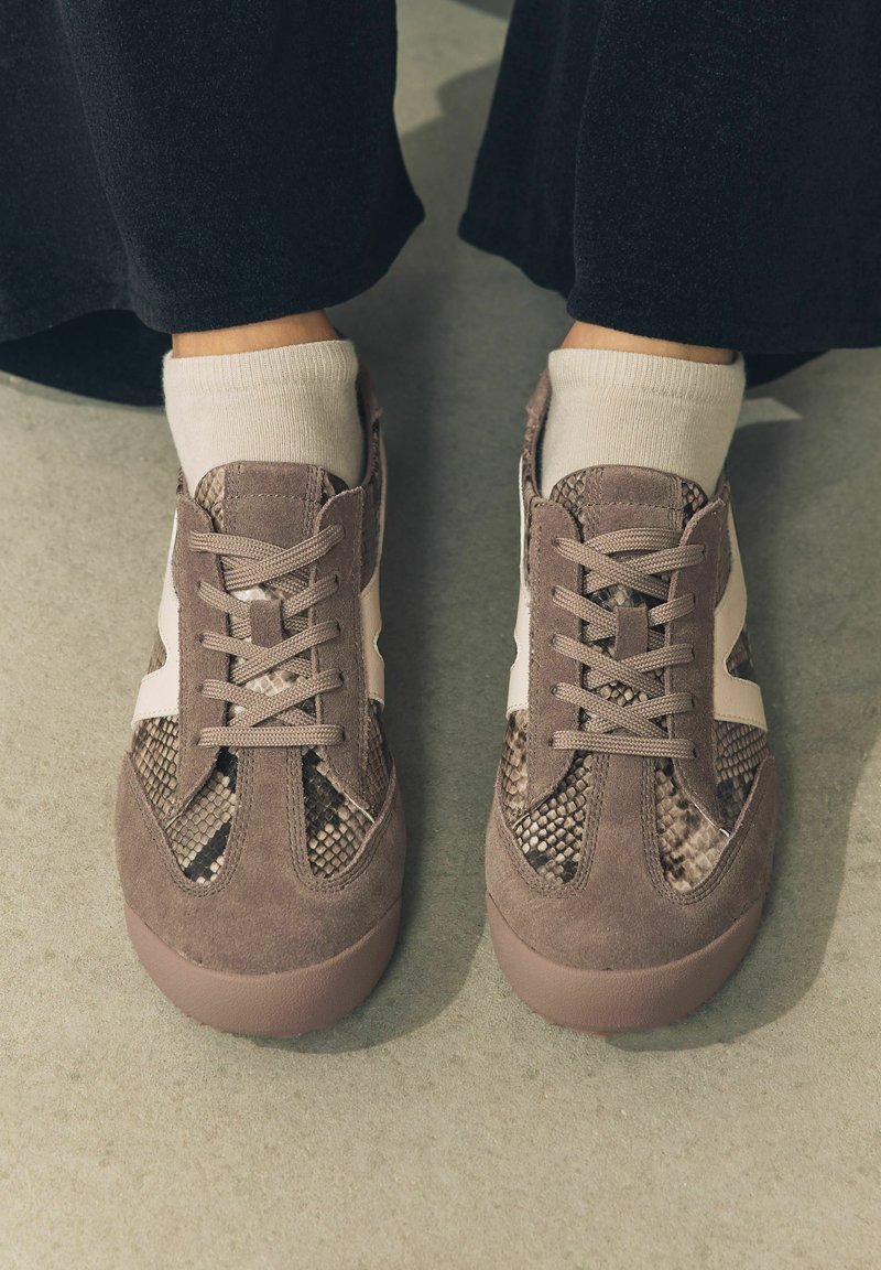 Sneaker mit einer Kombination aus strukturiertem Schlangenprint und weichem grauen Wildleder, ausgestattet mit einem hellbeigen Akzentstreifen, flachen Schnürsenkeln und einer Gummisohle.