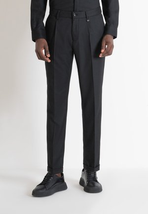 Pantalones negros ajustados con una textura suave, que cuentan con pliegues frontales y un corte ceñido. Combinados con zapatillas negras texturizadas.