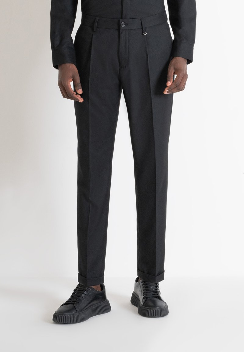 Pantaloni neri su misura con una trama liscia, caratterizzati da pieghe frontali e una vestibilità slim. Abbinati a sneaker nere con texture.