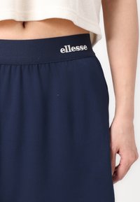Jupe de sport bleu marine fabriquée en tissu lisse, avec une taille élastique arborant le logo blanc "ellesse". Légère et ample.