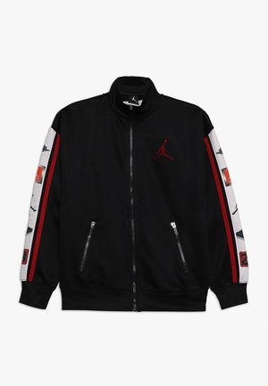 Veste noire à fermeture éclair avec des manches rayées rouges et blanches comportant divers logos, dont un logo Jumpman rouge sur la poitrine.