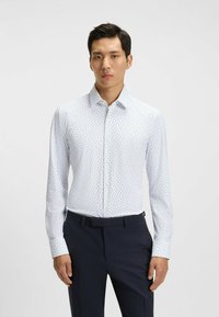 Vit långärmad skjorta med knappstängning och små bl åa bladmönster, figursydd passform och en välstruken krage, tillsammans med mörka byxor.