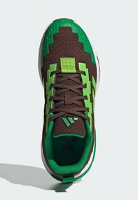 Hnedé tenisky s zelenými pixelizovanými akcentmi, textúrovanou tkaninou a bielou podrážkou. Obsahujú digitálny dizajn na špičke a zelenú podšívku.