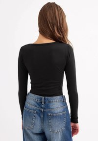 Top negro de manga larga con escote redondo, combinado con vaqueros azul de cintura alta que cuentan con dos bolsillos traseros y una textura clásica de denim.