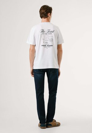 White cotton t-shirt with a graphic print on the back, featuring a cartoon toast and jar. Paired with dark blue jeans and brown shoes.