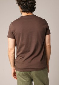 T-shirt en coton marron avec un col rond classique, des manches courtes et une coupe ajustée. Texture lisse, sans motifs ni accents visibles.