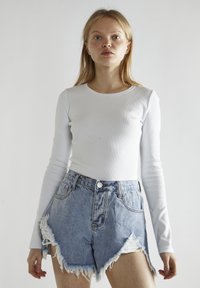 Top blanco de manga larga y canalé combinado con unos pantalones cortos de mezclilla de tiro alto, desgastados y con bordes deshilachados, que cuentan con un cierre de botón.