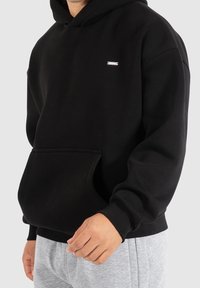 Černá mikina s kapucí vyrobená z bavlněné směsi, s přední klokaní kapsou a ribbovanými manžetami. Minimalistický design s jemným brandováním.