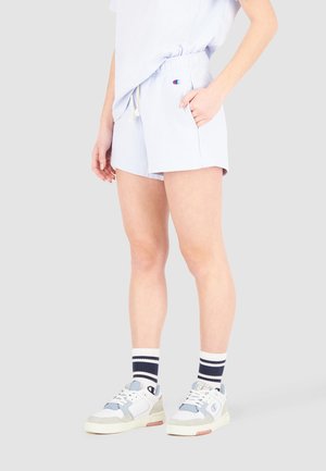 Lyseblå sportsshorts med elastisk talje, snørre, sidelommer og et lille logo på forsiden. Båret med hvide sneakers og stribede sokker.