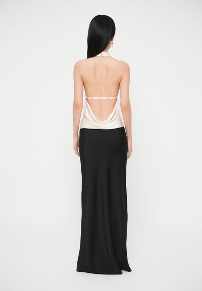 Saténový krémový top s preloženým chrbtom, v kombinácii s priliehavou čiernou sukňou dĺžky po zem. Má nastaviteľné ramienka a hladké textúry.