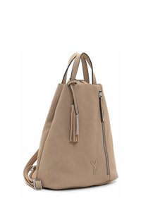 Beige texturerad ryggsäck av perforerat material. Har en sidodragkedja, två korta handtag, en lång justerbar rem och tofsdetalj.