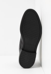 Černá podrážka boty s texturovaným povrchem. Obsahuje značkové a velikostní označení. Materiál se zdá být guma s propracovanými vzory běhounu.