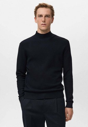 Suéter negro de cuello alto en textura acanalada con mangas largas, silueta ajustada y complementado con pantalones oscuros.