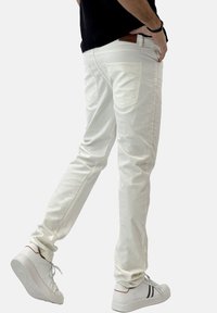 Pantalones de algodón blancos con corte ajustado, bolsillos delanteros y traseros, textura suave y costuras sutiles. Llevados con zapatillas blancas con detalles en negro.