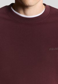 Μπορντό φούτερ με στρογγυλή λαιμόκοψη και λεπτή ραβδωτή υφή. Διαθέτει διακριτικό λογότυπο Lyle & Scott σε πιο ανοιχτή απόχρωση.