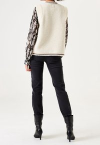 Krämfärgad faux shearling-väst med en kontrasterande svart och vit mönstrad långärmad skjorta under, tillsammans med mörka jeans och svarta klackstövlar.