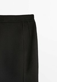 Tissu polaire noir avec couture visible et taille sur pantalon ou jupe à coupe droite sur fond blanc.