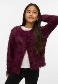 Vīna sarkanas mākslīgās kažokādas kardigans ar garām piedurknēm, apaļu kakla izgriezumu un pogu aizdari. Valkāts pār baltu topu, kombinēts ar melnām biksēm.