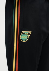 Sorte bukser med vertikale grønne, gule og røde striper og en logo-lapp fra Jamaica Football Federation på øvre lår.