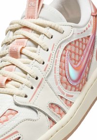 Vita sneakers med rosa accenter, tygnätöverdrag, iriserande swoosh och texturerade detaljer. Har krämfärgade snören och rosa stickmönster.