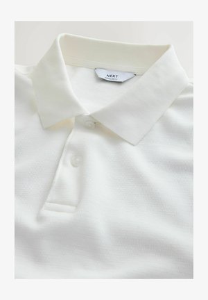 Valkoinen kauluksellinen poolopaita, jossa on kaksi nappia ja näkyvä "NEXT Regular Fit" -etiketti kaula-aukon sisäpuolella.