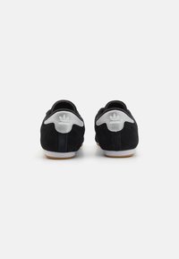 Black suede athletic shoes with gray accents, featuring a rubber sole and logo detail at the heel. Rounded shape, minimal design.