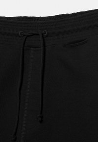 Talie de pantalonii de trening negri cu canelură elastică, șnur legat în nod și un mic buzunar frontal vizibil aproape de partea de sus dreapta.