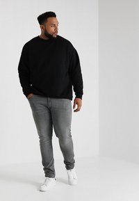 Sudadera negra, jeans grises y zapatillas blancas. La sudadera es de corte holgado; los jeans son ajustados con acabado desgastado.