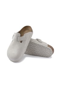 Zoccoli in suede grigio chiaro con punta arrotondata, cinturino regolabile e suola in gomma testurizzata con motivo a onda.