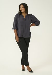 Blusa grigia scura con motivo a pois testurizzato, scollo a V e maniche a palloncino, abbinata a pantaloni neri aderenti e décolleté nere punti.