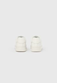 Adidași din piele albă cu design cu talpă joasă, textură netedă, accente minimaliste și cârlige rotunjite la călcâi. Estetică simplă și curată.