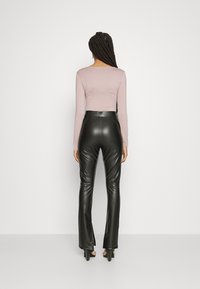 Blusa rosa de manga longa e calças pretas de imitação de couro flared com uma cintura alta, apresentando uma textura suave e uma silhueta ajustada.