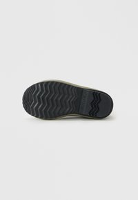 Suela de goma negra con patrón de zigzag y el nombre de la marca "SOREL" grabado cerca del talón, mostrado sobre un fondo blanco liso.