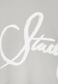 Texte cursif blanc « Start » sur un fond en tissu texturé gris clair, montrant une partie d'un design imprimé plus grand.