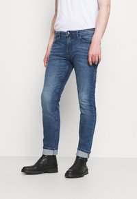 Blå denim skinny jeans med en blekt finish, med en klassisk femfickdesign och uppvikta benslut, kombinerat med svarta ankelboots.