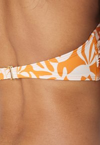 Top bikini arancione e bianco con motivo floreale, tracolla regolabile con accessori in oro, realizzato in tessuto morbido e elastico.