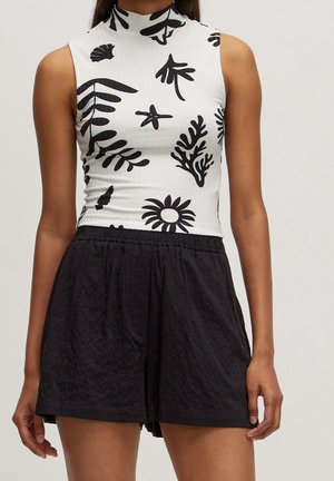 Haut blanc sans manches avec imprimés abstraits de feuilles et de fleurs noirs, associé à un short noir ample taille haute porté par une personne.
