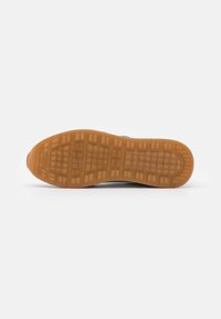 Suola di una scarpa, realizzata in gomma con un motivo di presa testurizzato, caratterizzata da un colore marrone chiaro traslucido e un design del battistrada dettagliato.