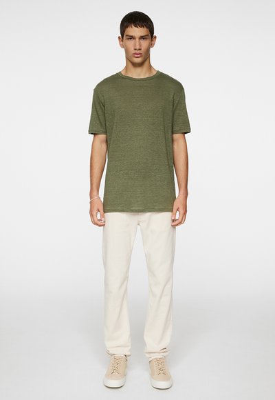 T-shirt vert olive à manches courtes en tissu texturé, associé à un pantalon blanc cassé et des baskets beiges. Design simple et coupe décontractée.