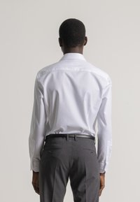 Camisa blanca de manga larga combinada con pantalones grises. La camisa tiene un cuello clásico y puños abotonados, mientras que los pantalones tienen una textura suave.