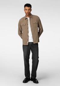 Brun knappeskjorte med to brystlommer, kombinert med mørke jeans og svarte sko. Det glatte stoffet og den skreddersydde passformen forbedrer det totale utseendet.