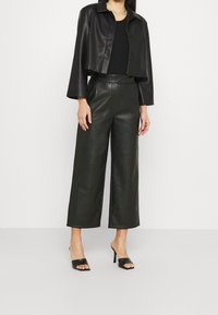 Giubbotto cropped in pelle nera con colletto, abbinato a pantaloni larghi in pelle nera a vita alta e mules con tacco aperti neri.