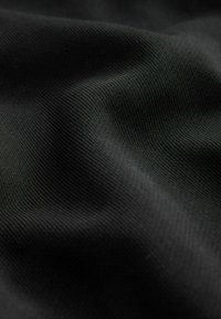 Tejido sintético negro con una superficie lisa y ligeramente texturizada, que presenta sutiles ondulaciones y pliegues que indican flexibilidad.